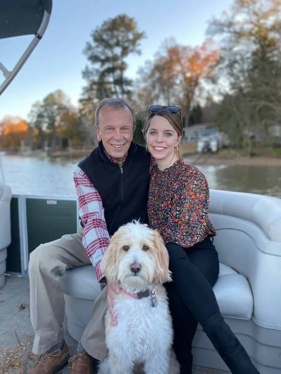 Shelby on the boat with family and their goldendoodle, autumn trees along the lake