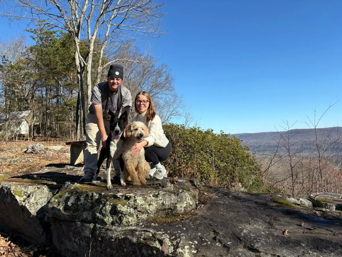 Shelby and Hobey crouched on a rock ledge with their two dogs, mountains behind